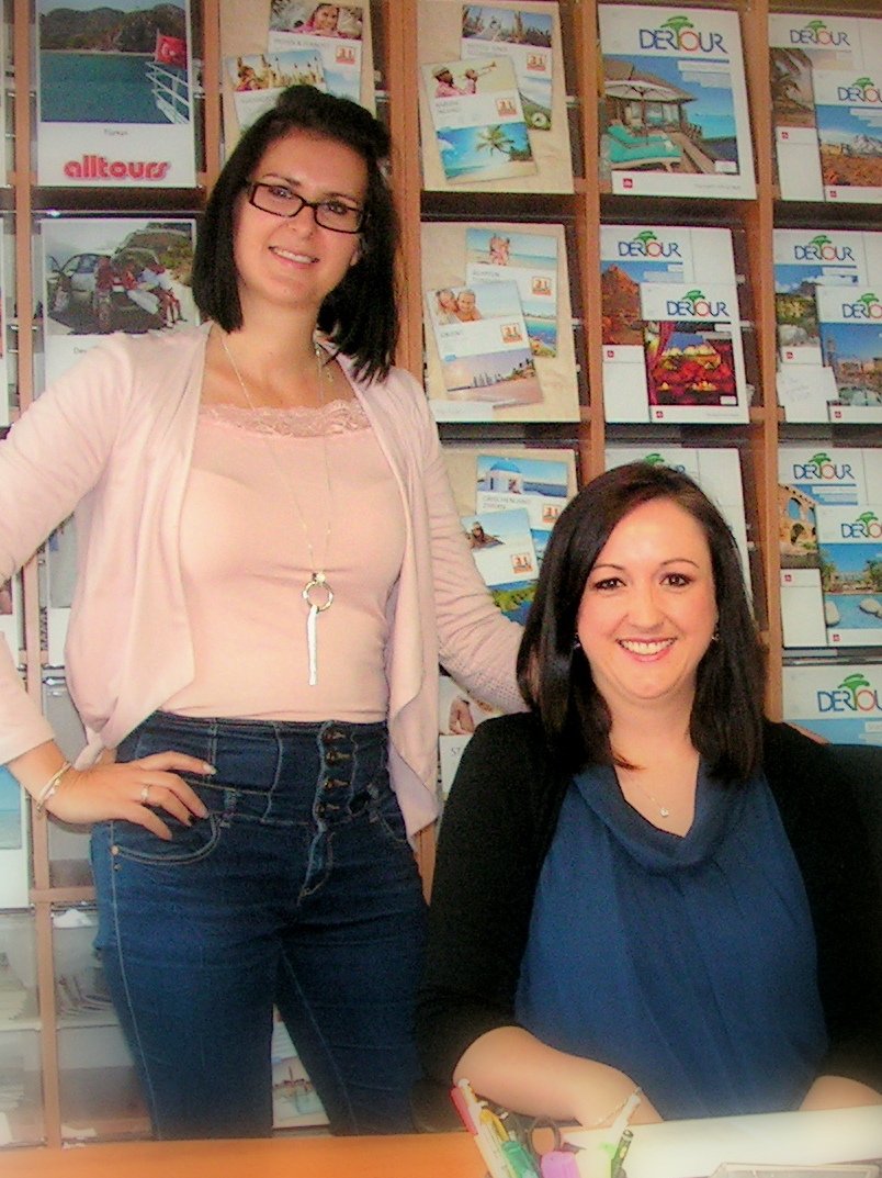 Loreen Hoffmann und Sabine Schlittenbauer im Reisebüro vor der Katalogwand mit alltours- und DERTOUR-Reisekatalogen